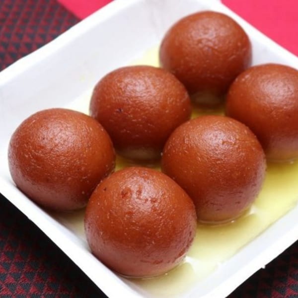 Six gulab jamun, Indian fried dough balls soaked in syrup, in a white dish.