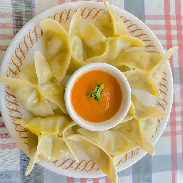 A plate of Indian momos, steamed dumplings, arranged around a small bowl of orange dipping sauce.
