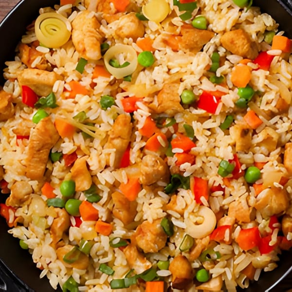 Close-up of Indian chicken fried rice with peas, carrots, and bell peppers in a black bowl.