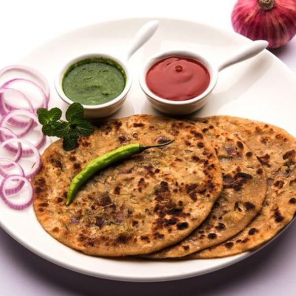 Three Indian parathas with green chili, mint, red onion, green chutney, and red sauce.