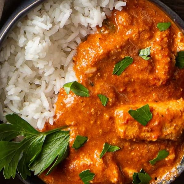Close-up of Indian butter chicken with white rice and fresh parsley in a dark bowl.